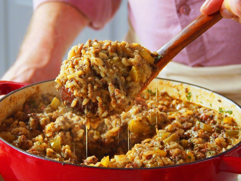 Eine Pfanne Cajun Style Dirty Reis, aus der mit einem Löffel eine Portion entnommen wird.