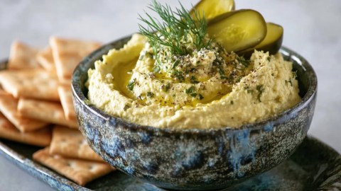 Eine Schale Dillgurken-Hummus. Dahinter liegen Cracker.