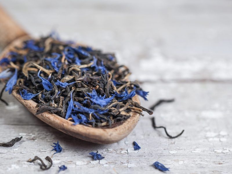 Earl Grey selbst machen: Ein Löffel Earl Grey mit Kornblumenblüten liegt auf einem hellen Holztisch.