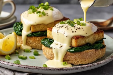 Zwei vegane Eggs Benedict mit Sauce hollandaise auf einem Teller.