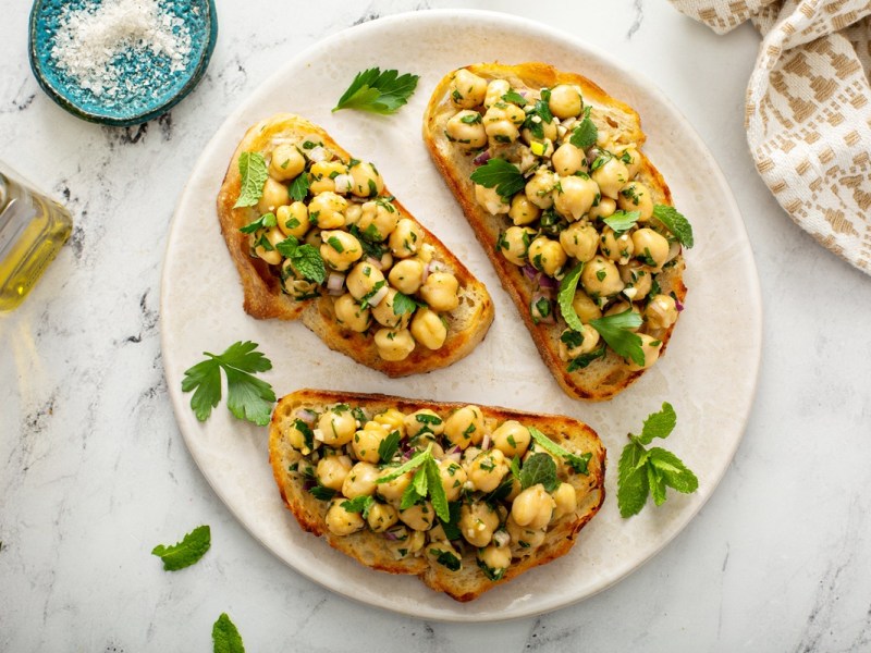 Drei Scheiben Kichererbsen-Bruschetta auf einem hellen Teller.