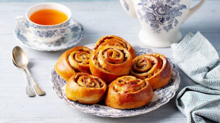 Nussschnecken auf einem gemusterten Teller. Dahinter eine Tasse Tee.