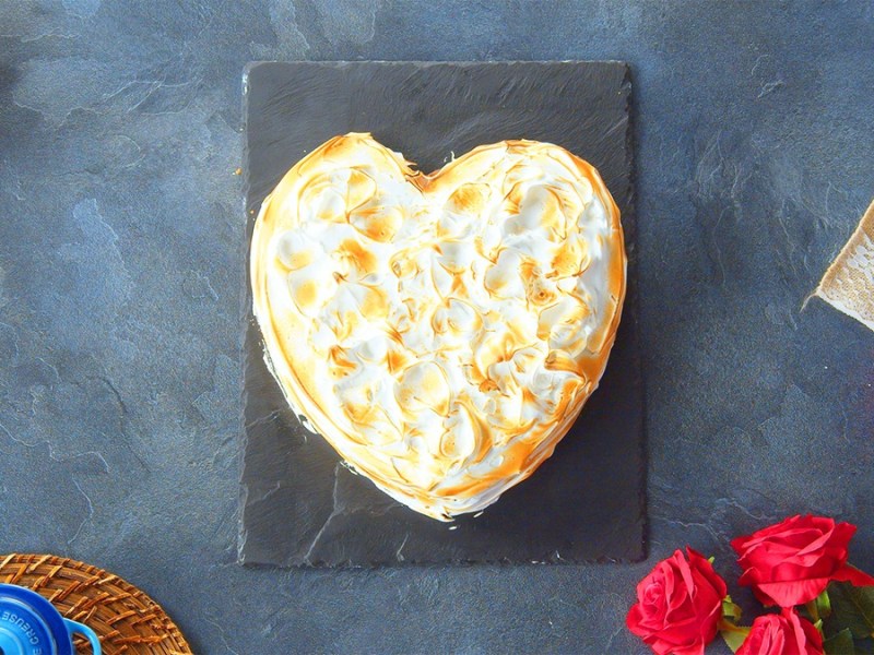 Ein Omelette SUrprise liegt auf einer Schieferplatte auf einer grauen Arbeitsplatte. Unten links im Bild steht eine Tasse und es liegt ein Küchentuch darüber. Oben links im Bild ist eine Rose. Rechts im Bild liegen weitere Rosen sowie eine Dose.