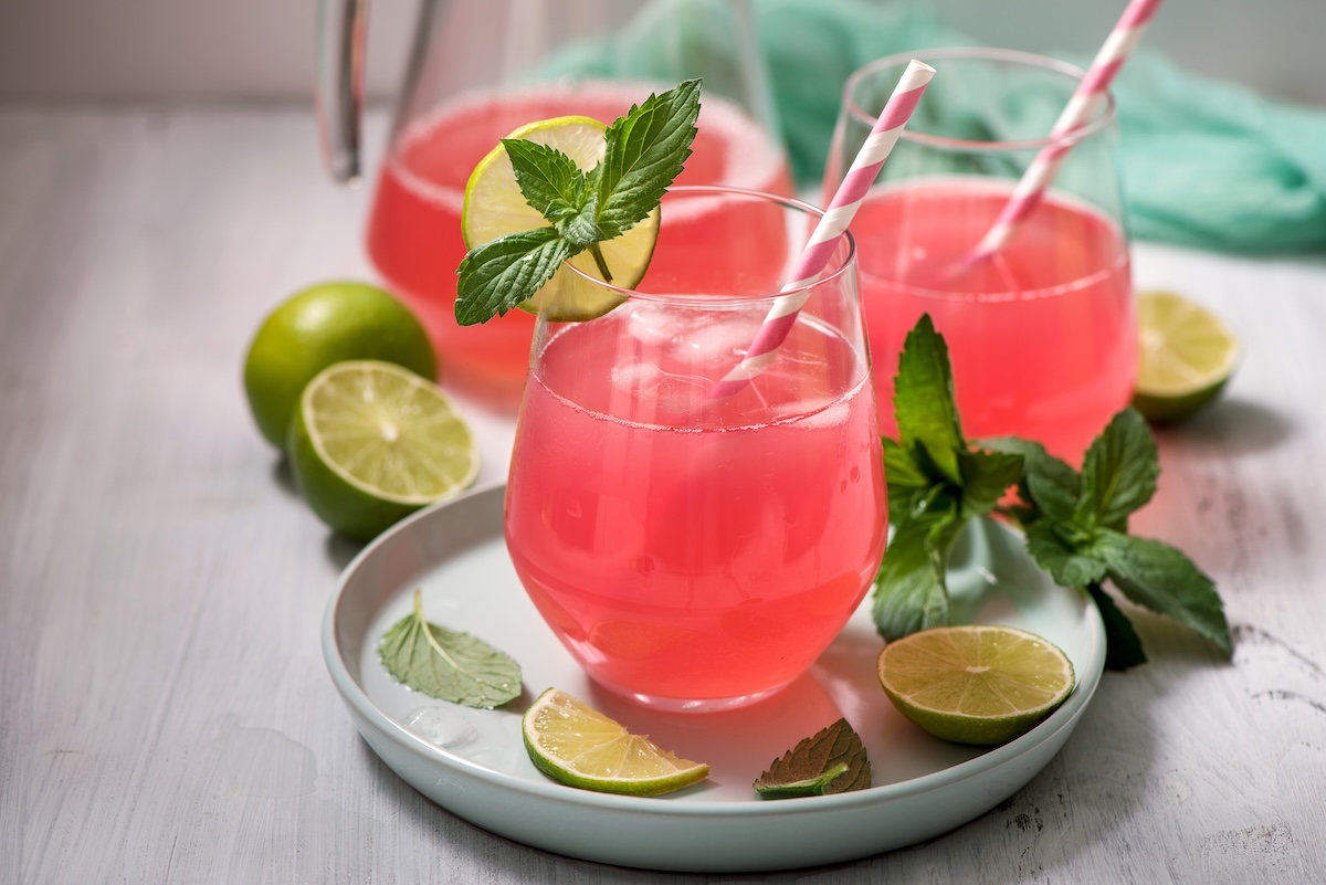 3 Gläser Rhabarber-Holunder-Spritz mit Strohhalmen, garniert mit Minze und Limetten.