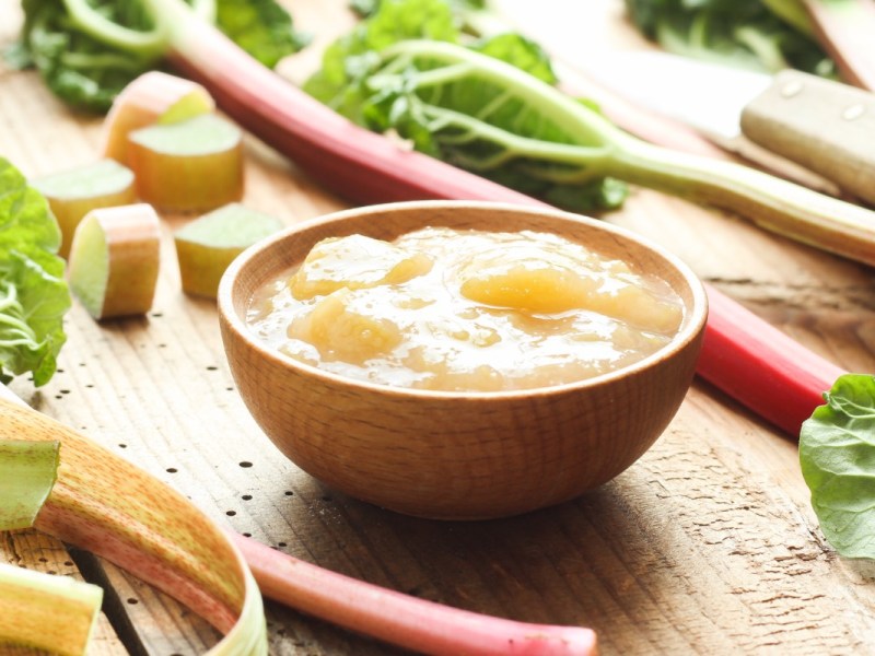 Eine Schale Rhabarbergrütze. Daneben liegen frische Rhabarberstangen.