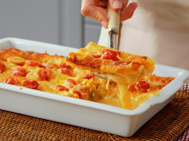 Ein Stück Spargel-Cannelloni-Auflauf wird mit einer Kelle über dem Auflauf gehalten.