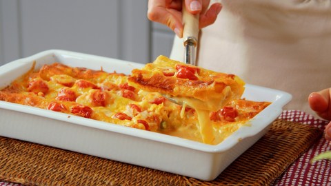 Ein Stück Spargel-Cannelloni-Auflauf wird mit einer Kelle über dem Auflauf gehalten.