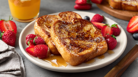Zwei vegane French-Toasts auf einem weißen Teller, angerichtet mit Ahornsirup und Erdbeeren.