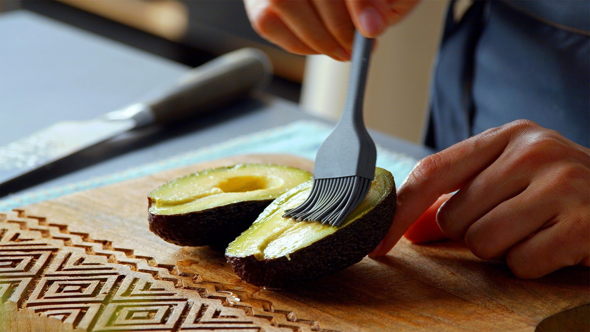 Zwei Acocadohälften auf einem Holzbrett. Sie werden von einer Köchin eingepinselt.