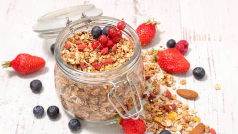 Ein Glas Beeren-Knuspermüsli, drum herum liegen frische Beeren.