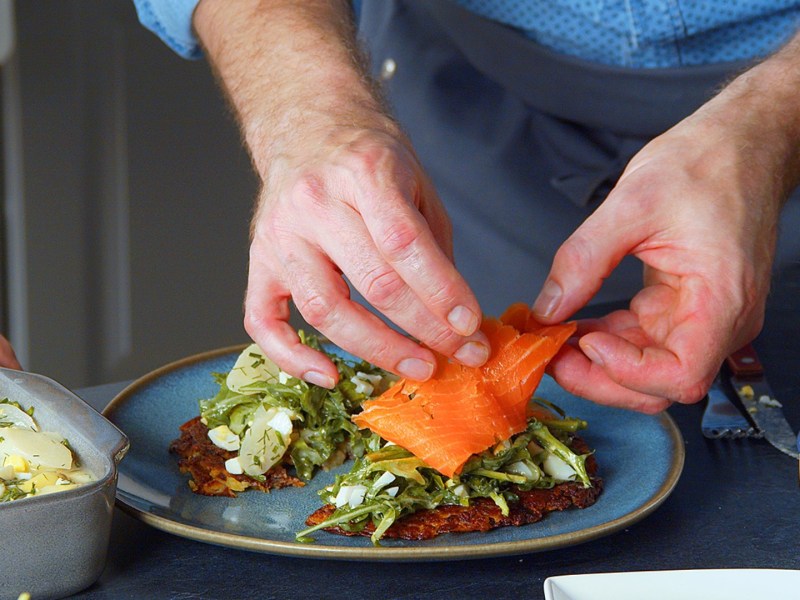 Berner Rösti mit Spargelsalat, auf die eine Scheibe Räucherlachs gelegt wird.