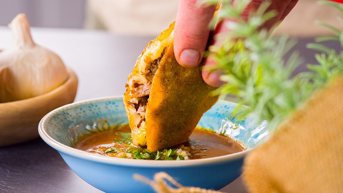 Birria-Tacco, der in Soße getunkt wird