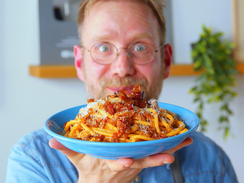 Koch Oli hält einen Teller mit Bucatini all'Amatriciana in die Kamera.
