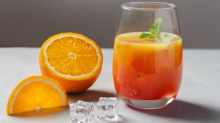 Ein Glas Campari Orange mit Minze. Daneben liegt eine halbe Orange.