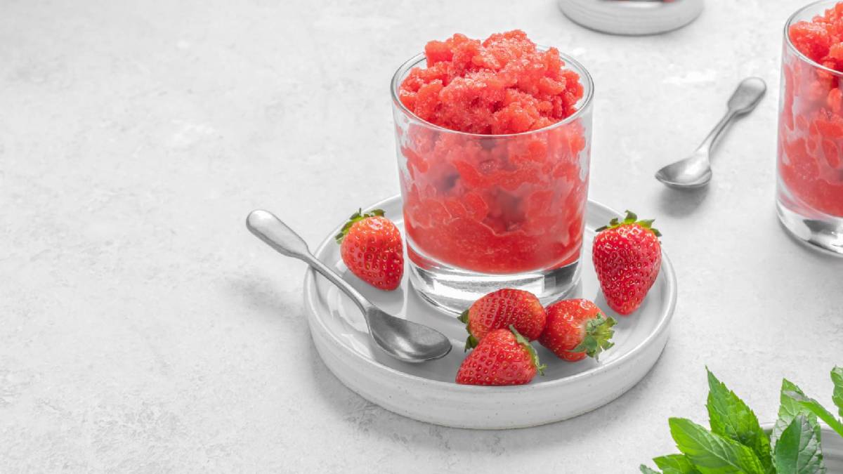 Ein Glas Erdbeer-Granita. Drum herum liegen Erdbeeren und Basilikumblätter.