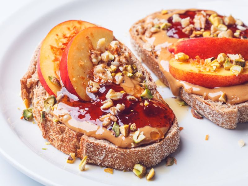 Zwei Scheiben Erdnussbutter-Pfirsich-Toast mit gehackten Nüssen und Marmelade.