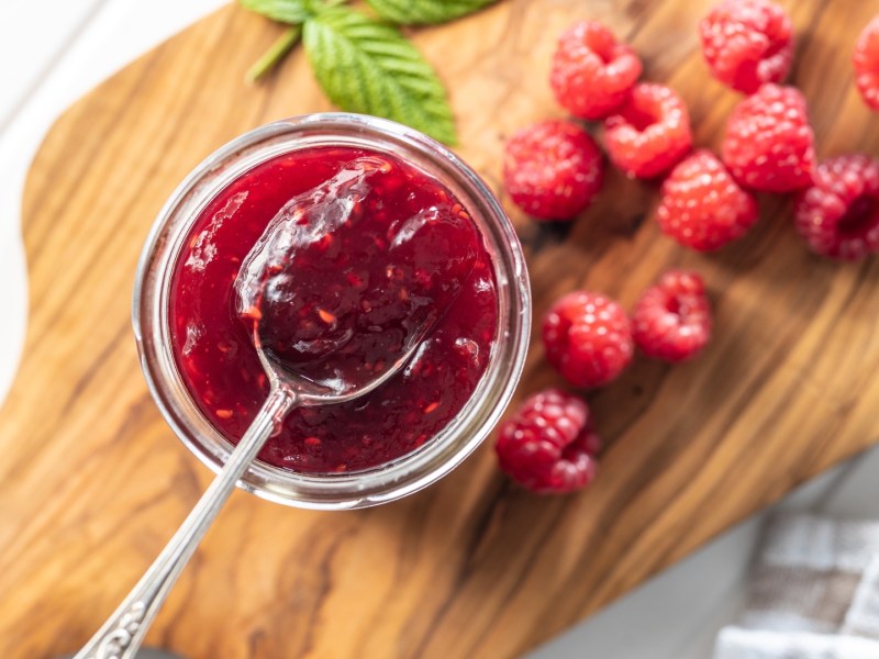 Ein Glas kaltgerührte Himbeerkonfitüre im Glas in der Draufsicht. Eine Löffel mit Konfitüre befindet sich über dem Glas.