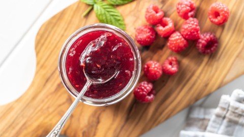 Ein Glas kaltgerührte Himbeerkonfitüre im Glas in der Draufsicht. Eine Löffel mit Konfitüre befindet sich über dem Glas.