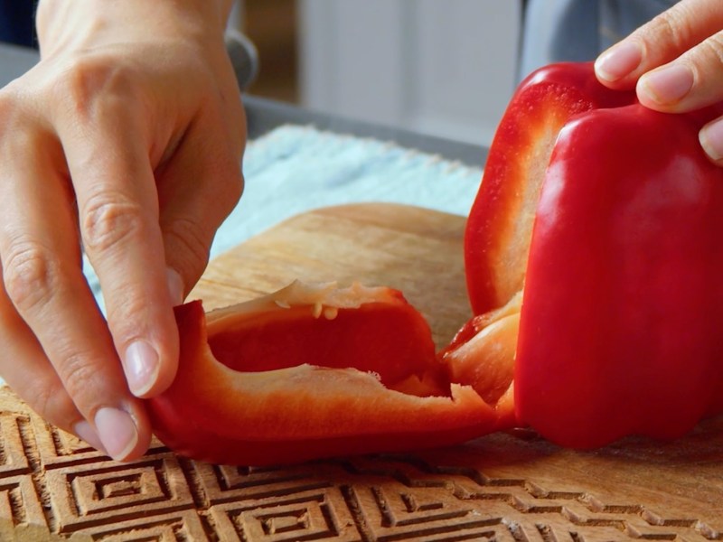 Paprika schneiden: Eine Köchin drückt eine Seite einer Paprika mit ihren Händen runter.