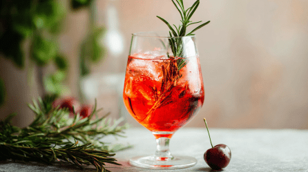 Ein Glas Savoia Spritz, garniert mit Rosmarin und einer Kirsche.