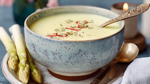 Eine Schüssel Spargel-Kokos-Suppe mit einem Löffel drin.