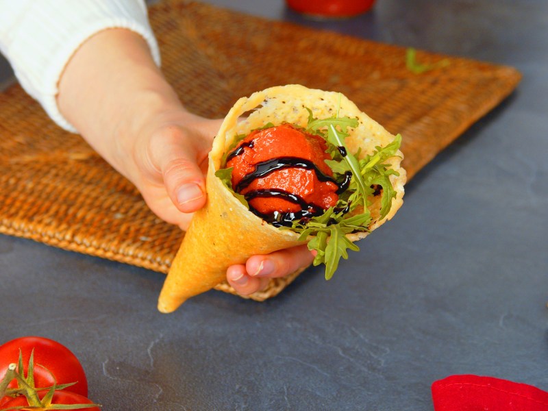 Eine Köchin hält eine Parmesanwaffel mit einer Kugel Tomatensorbet in die Kamera.