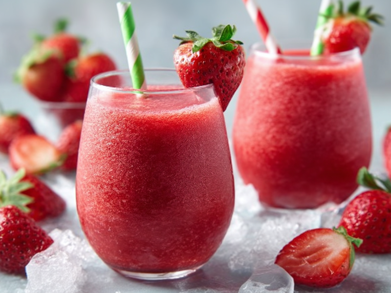 Zwei Gläser mit Wein-Slushy mit Erdbeeren sind zu sehen. Außen herum liegen Erdbeeren und Eiswürfel.