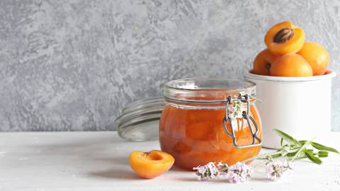 Glas Aprikosen-Lavendel-Marmelade mit frischen aprikosen daneben
