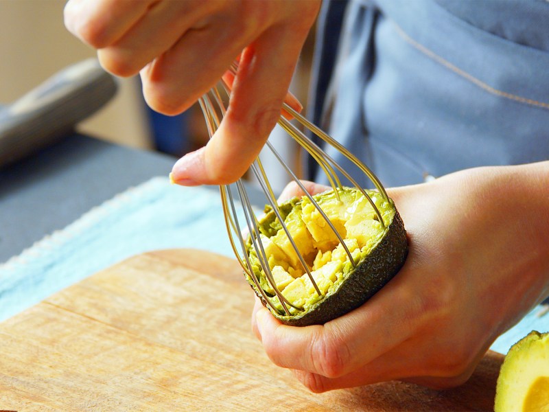Avocado aushöhlen: Eine Person höhlt eine Avocado mit einem Schneebesen aus.