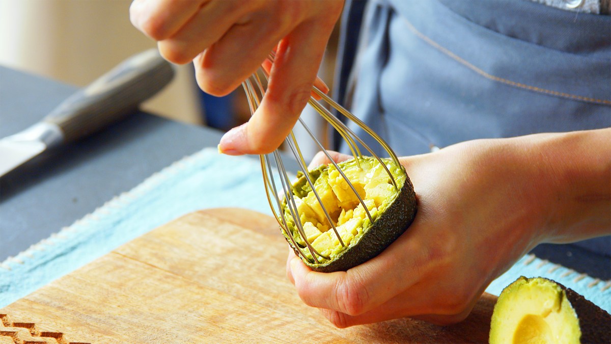 Avocado aushöhlen: Eine Person höhlt eine Avocado mit einem Schneebesen aus.