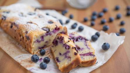 Blaubeer-Joghurt-Kuchen auf Backpapier mit zwei abgeschnittenen Stückchen.