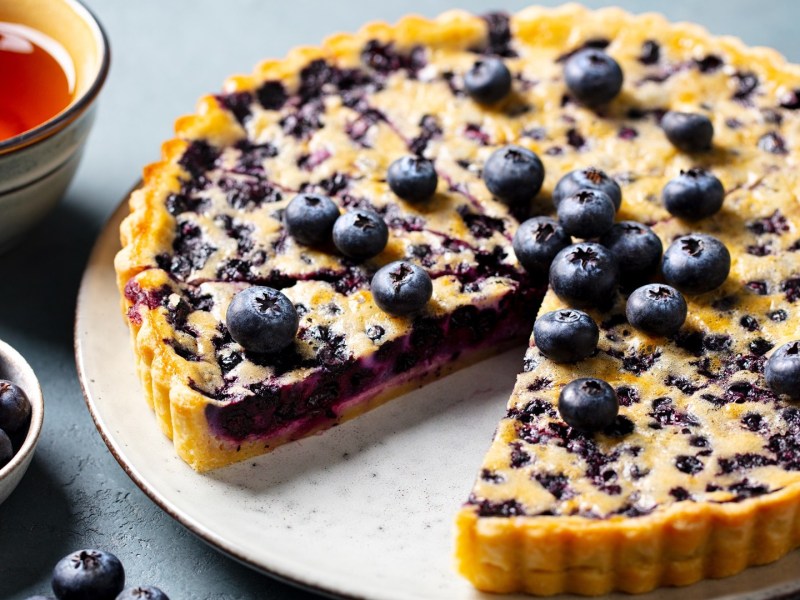 Eine Blaubeer-Vanille-Tarte, von der ein Stück entnommen wurde.
