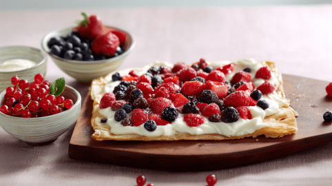 Flammkuchen mit Beeren, serviert auf einem Brett. Außen herum stehen Beeren auf einem Brett.