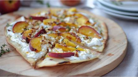 Brett mit einem in Stücke geschnittenen Flammkuchen mit Nektarinen und Ziegenkäse