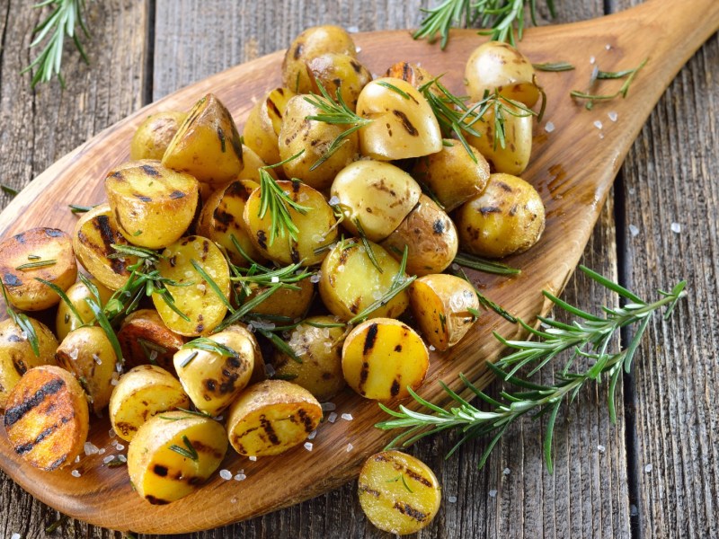 Eine große Portion gegrillte Kartoffeln mit Rosmarin auf einem Holzbrett.
