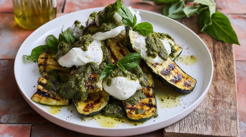 Gegrillte Zucchini mit Burrata und Pesto auf einem Teller mit hohem Rand.