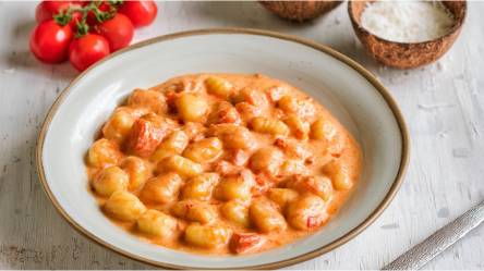 Ein Teller mit Gnocchi in Tomaten-Kokossoße auf einem Tisch, frische Tomaten daneben