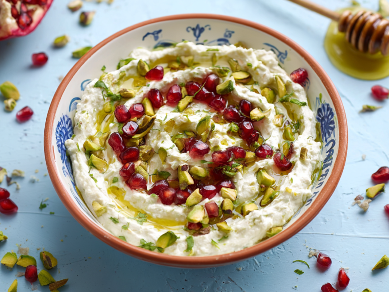 Granatapfel-Pistazien-Dip in einer Schüssel. Einzelne Granatapfel- und Pistazienkerne liegen als Deko um die Schale.