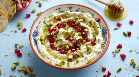 Granatapfel-Pistazien-Dip in einer Schüssel. Einzelne Granatapfel- und Pistazienkerne liegen als Deko um die Schale.