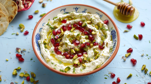 Granatapfel-Pistazien-Dip in einer Schüssel. Einzelne Granatapfel- und Pistazienkerne liegen als Deko um die Schale.