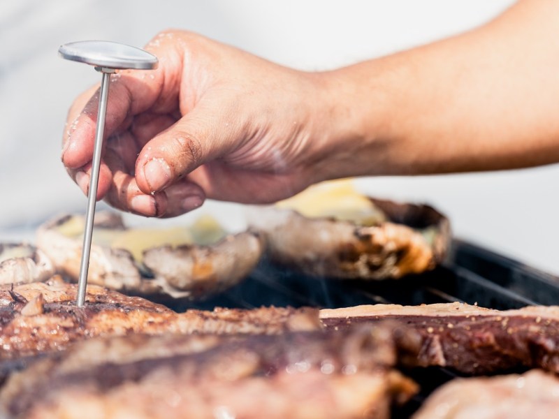 Ein Koch steckt ein Grillthermometer in ein Stück Fleisch.