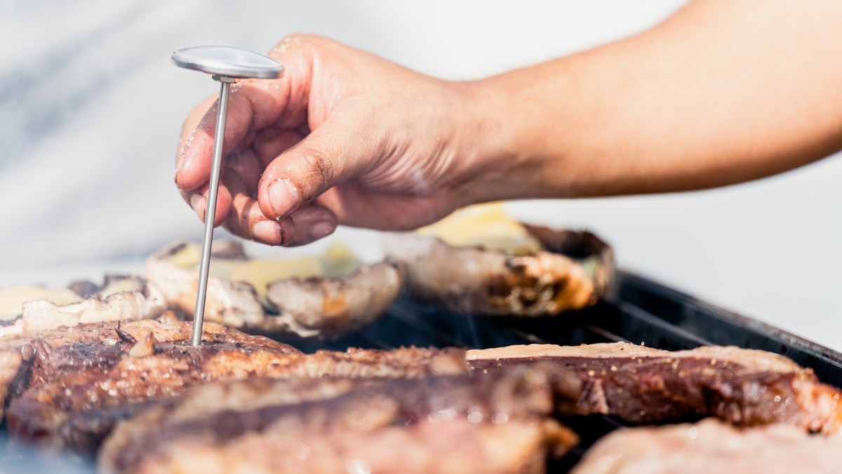 Ein Koch steckt ein Grillthermometer in ein Stück Fleisch.