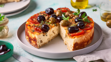 Herzhafter Cheesecake, dekoriert mit Oliven und Kräutern, steht angeschnitten auf einem Teller.