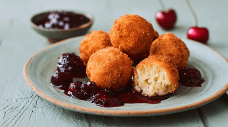 Milchreisbällchen mit Kirschkompott, serviert auf einem Teller. Kirschen und Kompott stehen im Hintergrund.