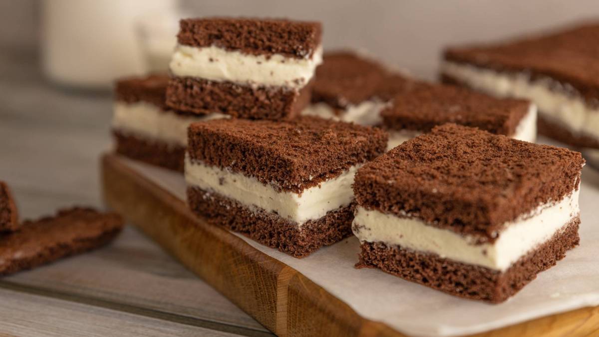 Ein Holzbrett, das mit Backpapier belegt ist und auf dem einige quadratische Stücke Milchschnitte-Kuchen liegen.