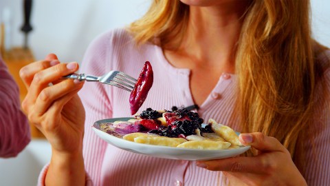 Nahaufnahme von Köchen Adrianne, die einen Teller mit Piroggi mit Vanille-Rahm und Heidelbeeren in die Kamera hält. In einer Hand hält sie eine Gabel mit einer Pirogge.
