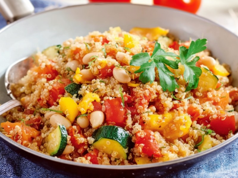 Eine Quinoa-Gemüse-Pfanne mit Zucchini, mit einem Löffel darin.
