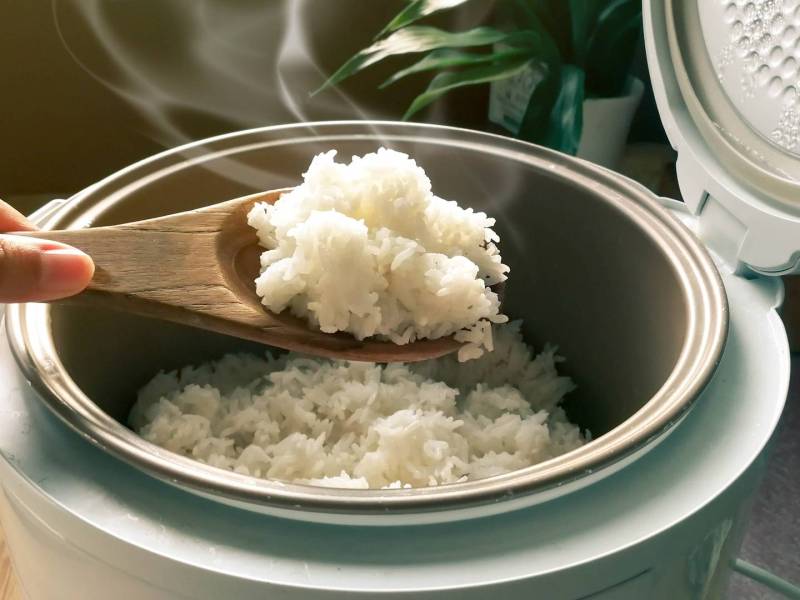 Ein Reiskocher, aus dem gerade mit einem Holzlöffel Reis geschöpft wird.