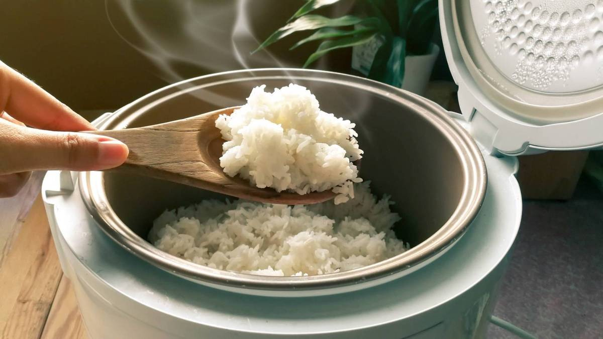 Ein Reiskocher, aus dem gerade mit einem Holzlöffel Reis geschöpft wird.