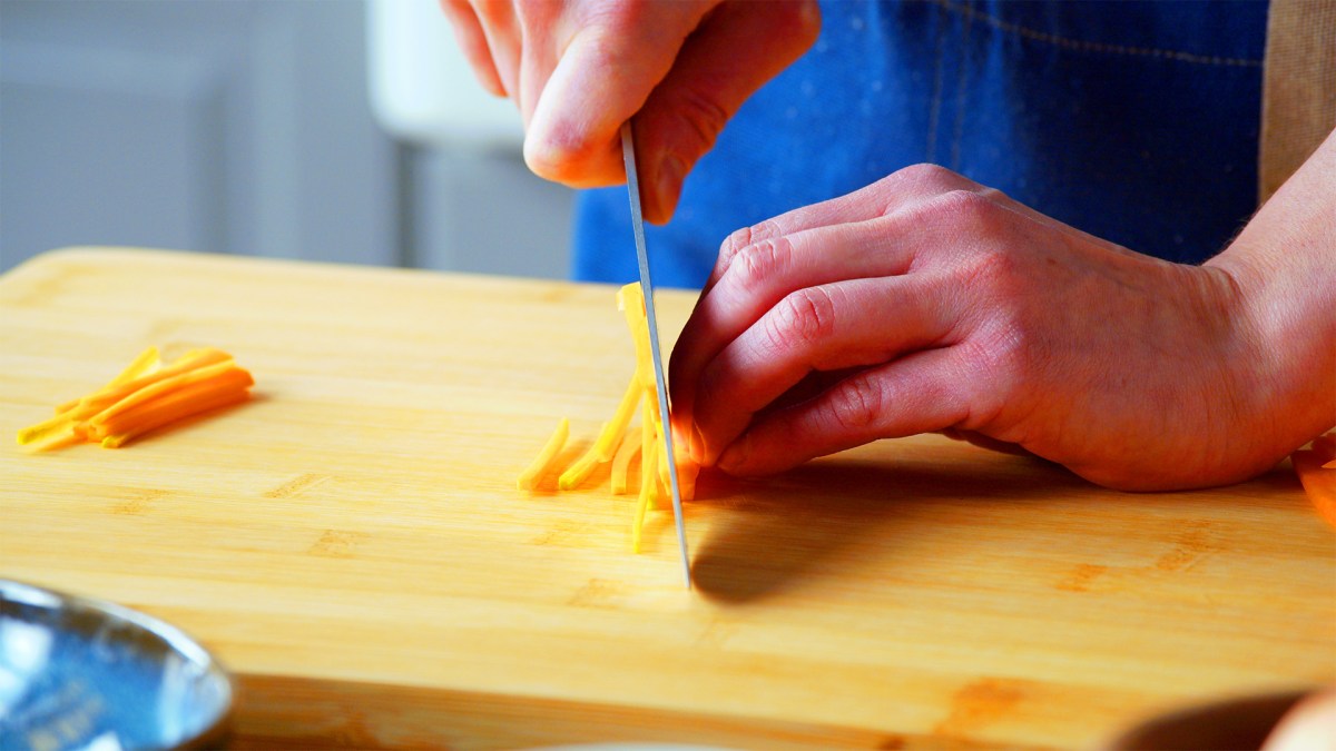 Schnittformen von Gemüse: Eine Köchin schneidet eine Möhre in dünne Streifen.